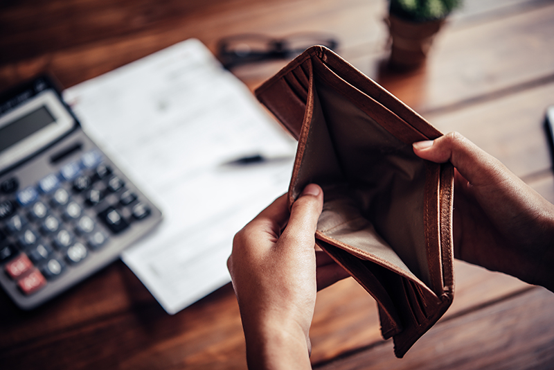 Person looking at an empty wallet with debt paperwork in background on the desk