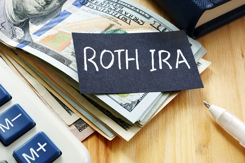 Roth IRA written on a piece of paper resting on a stack of money