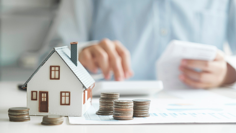 Man looking at house, money, and paperwork on a desk