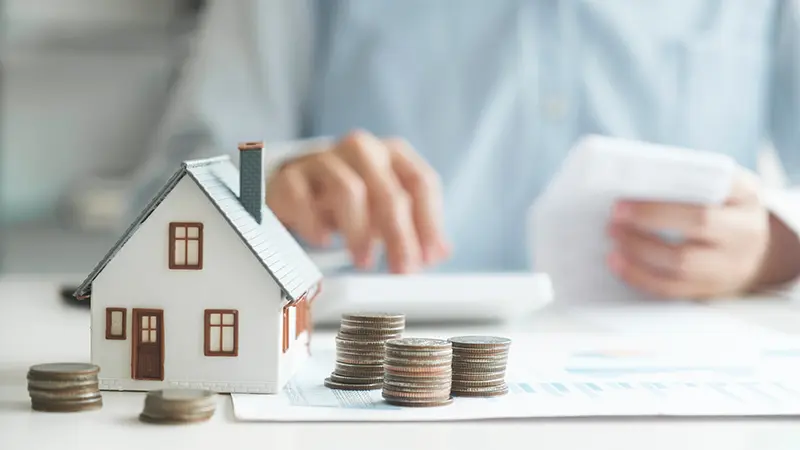 Man looking at house, money, and paperwork on a desk