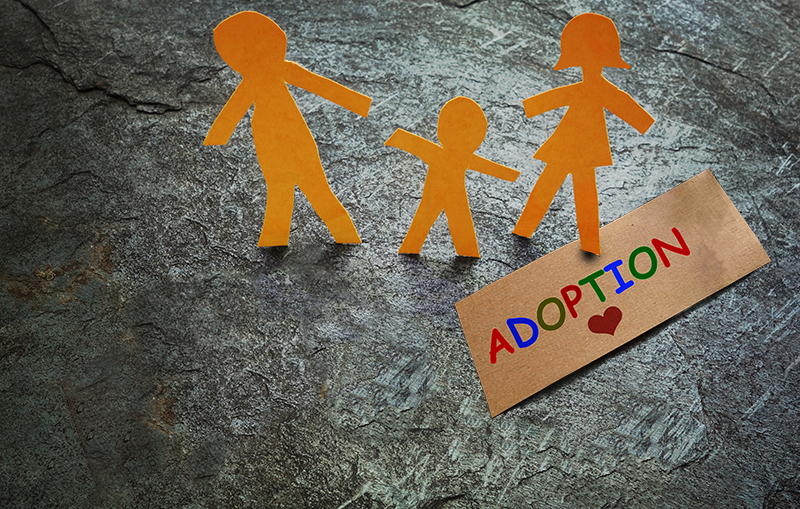 Man, child, and woman paper cutouts by an adoption sign