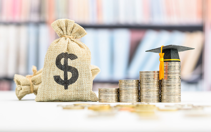 Bags of money and stacked coins with a graduation hat